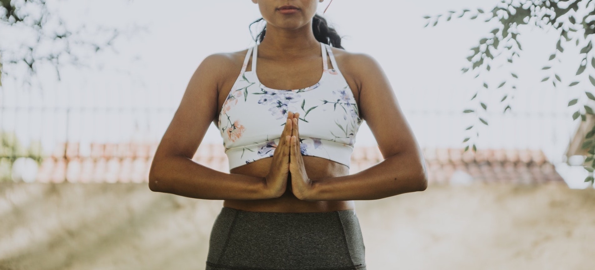 Woman practicing yoga in namaste pose with floral top and yoga pants